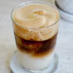 dalgona coffee in a clear glass with coffee foam and white milk layer