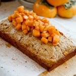 angled overhead shot of persimmon cake with chopped persimmons on top and stack of persimmons in the background