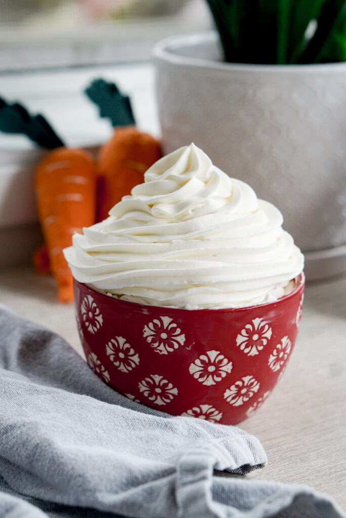 whipped cream cream cheese frosting in a red bowl with piped swirl on top