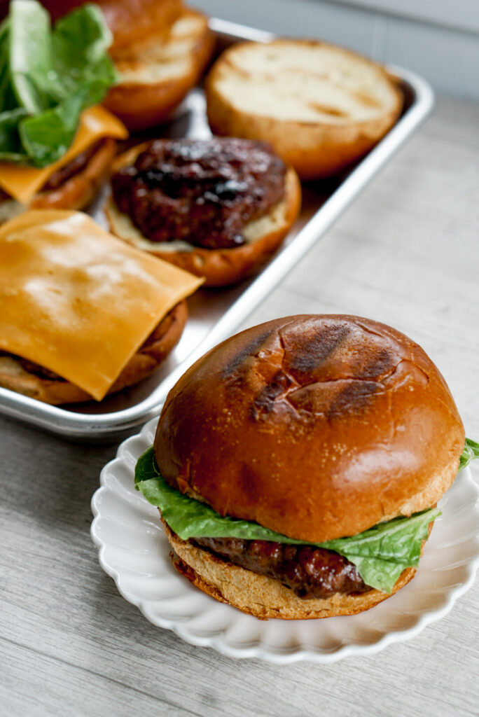 teriyaki burger angled shot with assembled burger and ingredients on a tray in the background