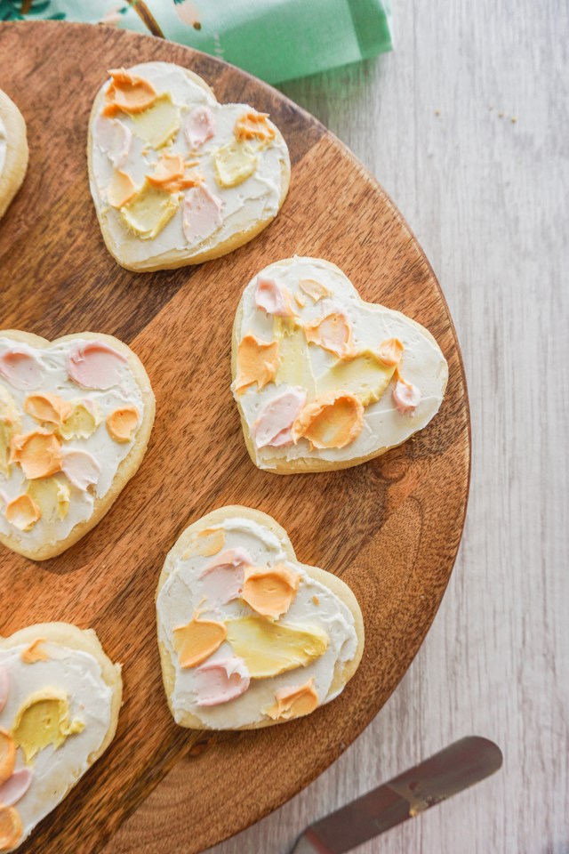Heart shaped cut out shortbread cookies with American buttercream frosting. The buttercream has a watercolor painted effect.