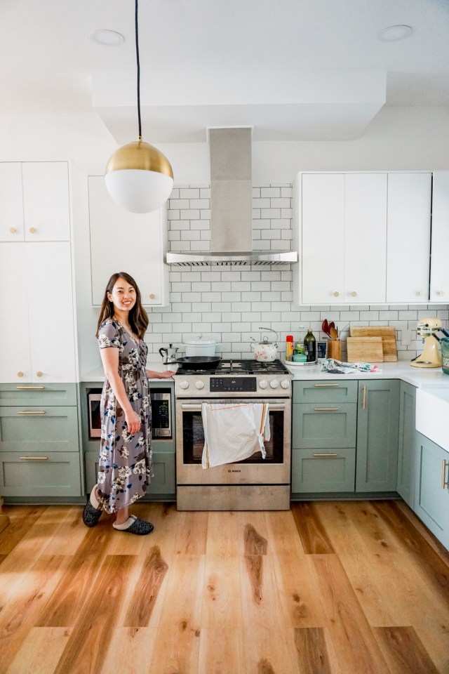 mid century modern kitchen renovation - two toned white and green cabinets, marble countertops, globe pendant light, gold hexagon knobs, and gold cabinet pulls