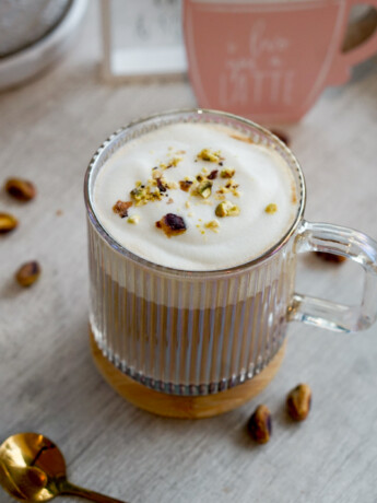 pistachio latte in clear mug with milk foam and chopped pistachios on top
