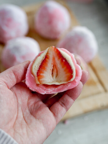 cross section of strawberry daifuku mochi with almond paste held in a hand